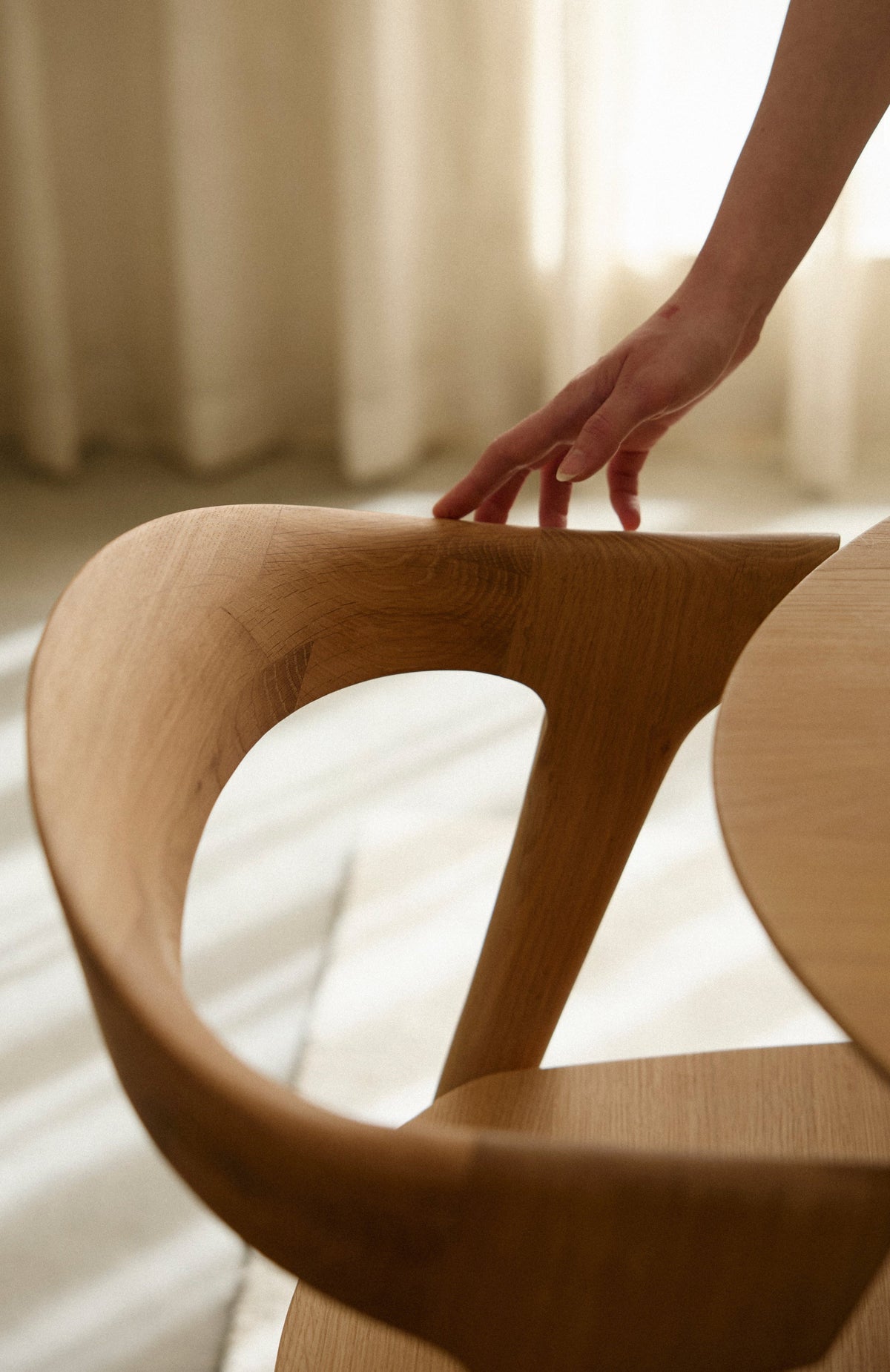 Wooden chair with a hand reaching towards it, soft lighting and blurred background